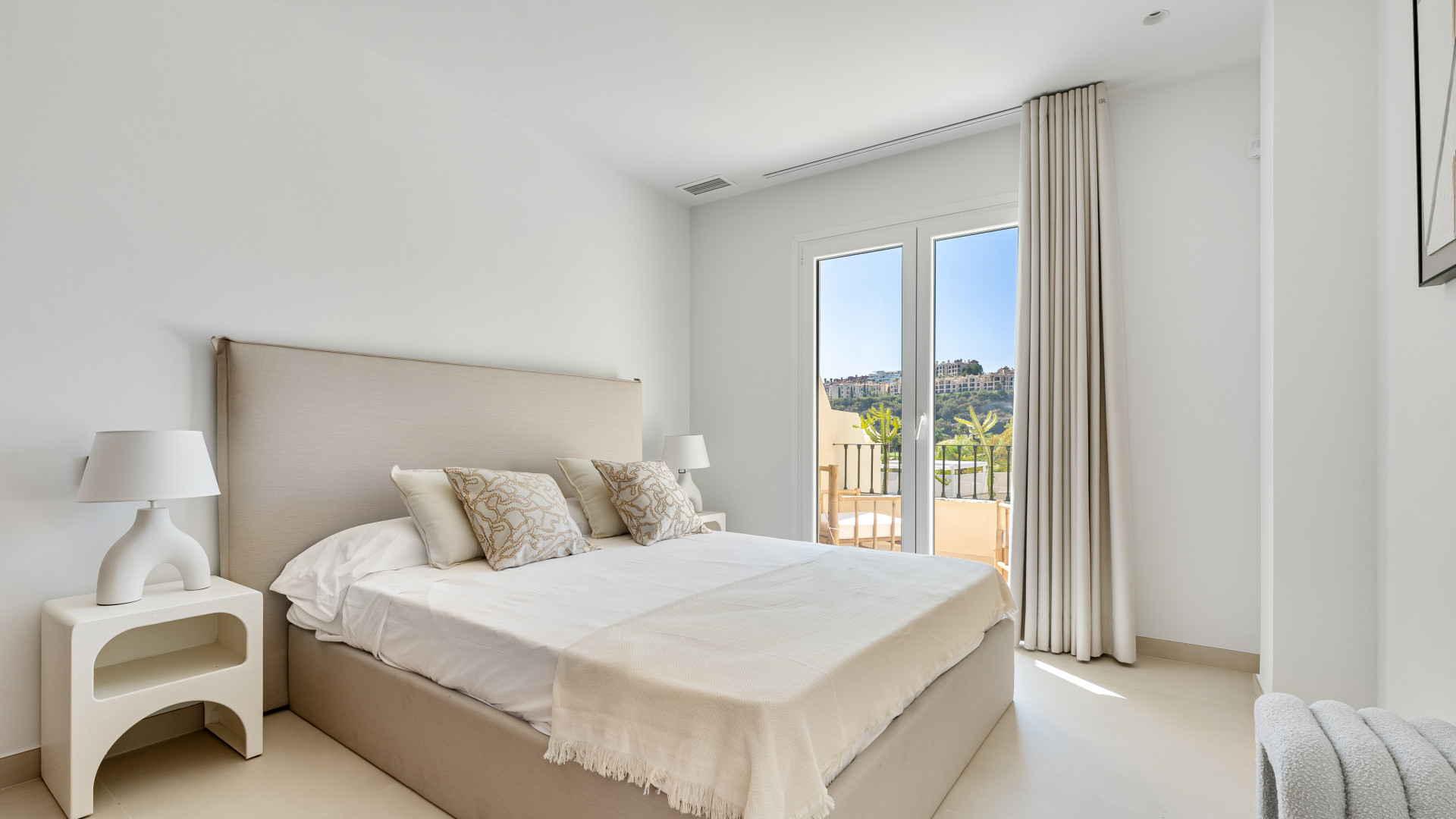 Bright bedroom featuring a bed with decorative pillows and balcony access.
