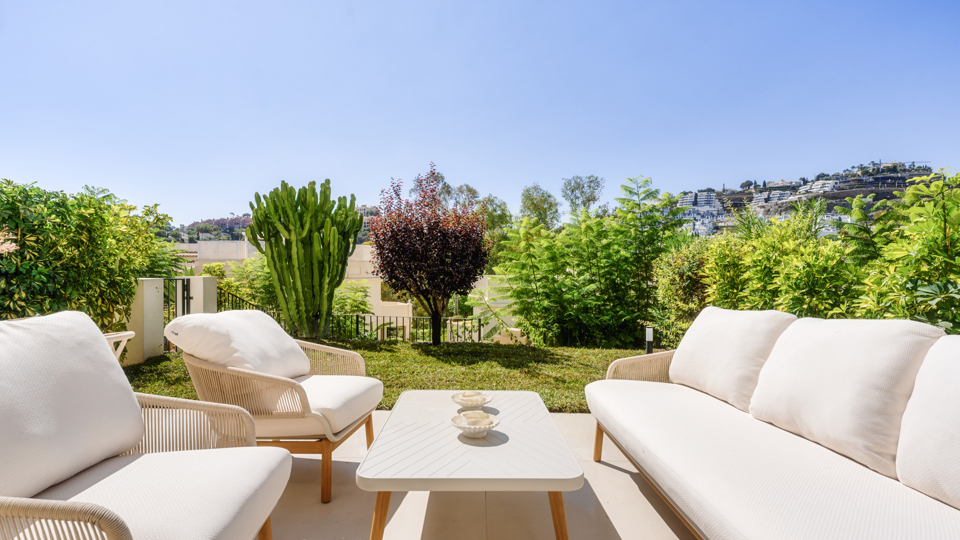 View from seating area showing garden greenery and decorative furniture against clear blue sky.
