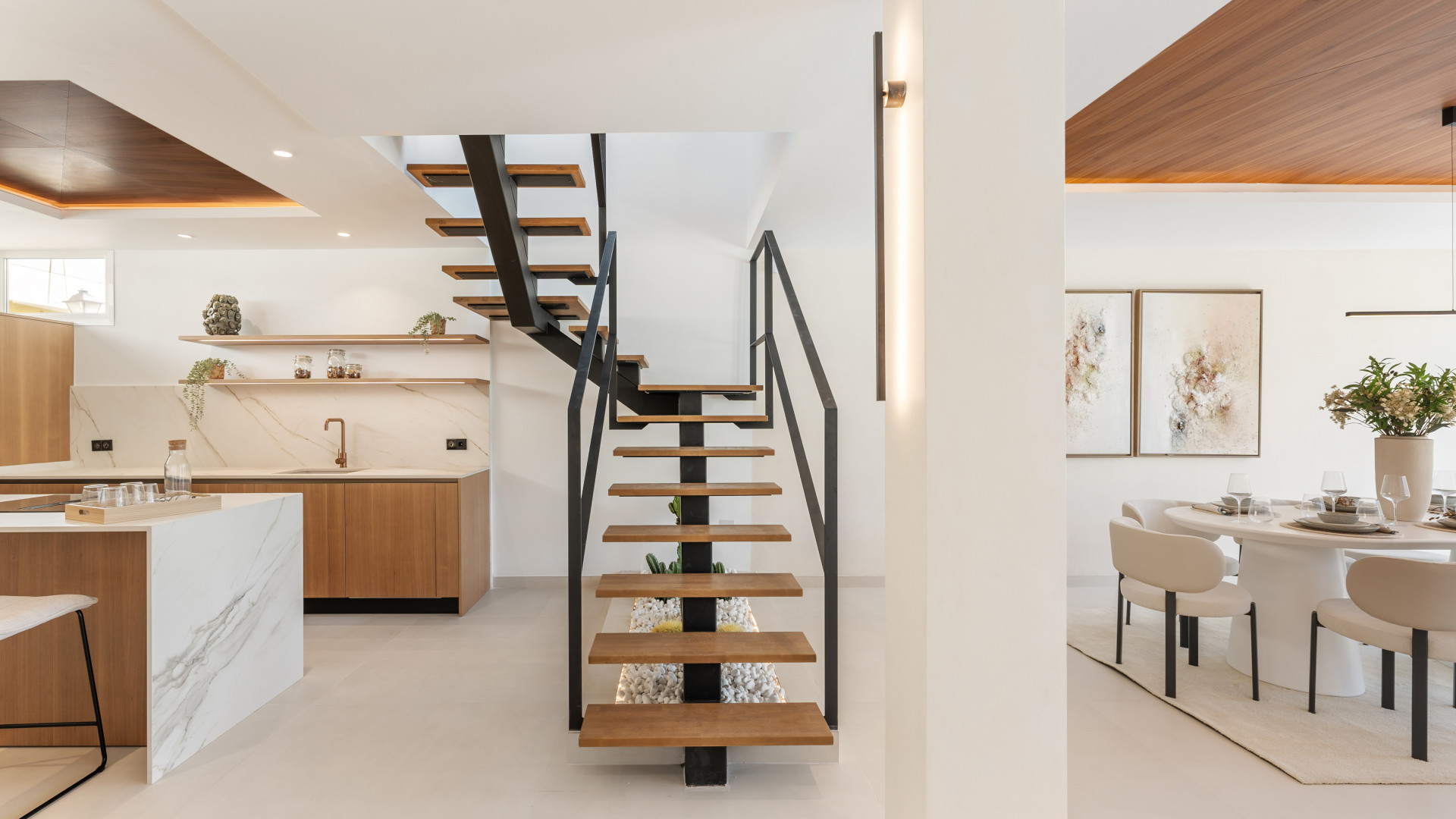 Interior view of the kitchen with open staircase and dining area featuring framed artwork.