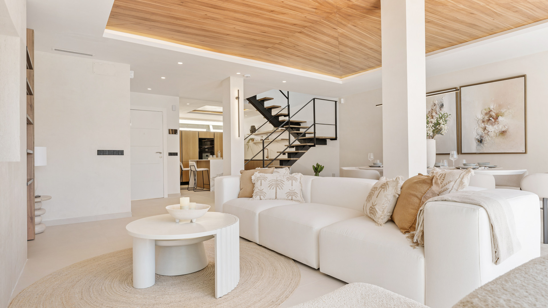 View of the living area with a sofa, round coffee table and wooden ceiling, staircase in the background.