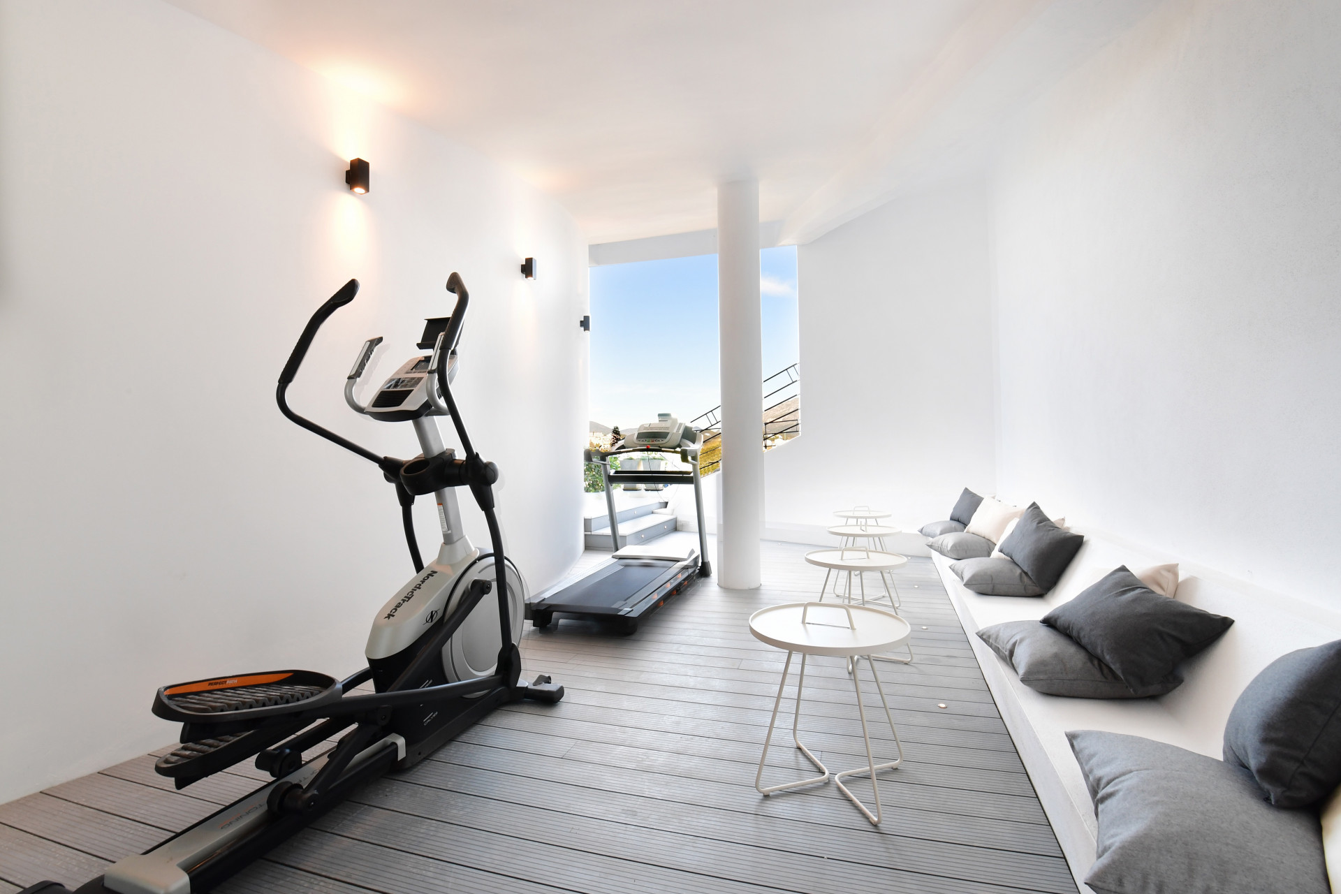 Bright gym area with elliptical and treadmill, white walls, modern decor, ample natural light.