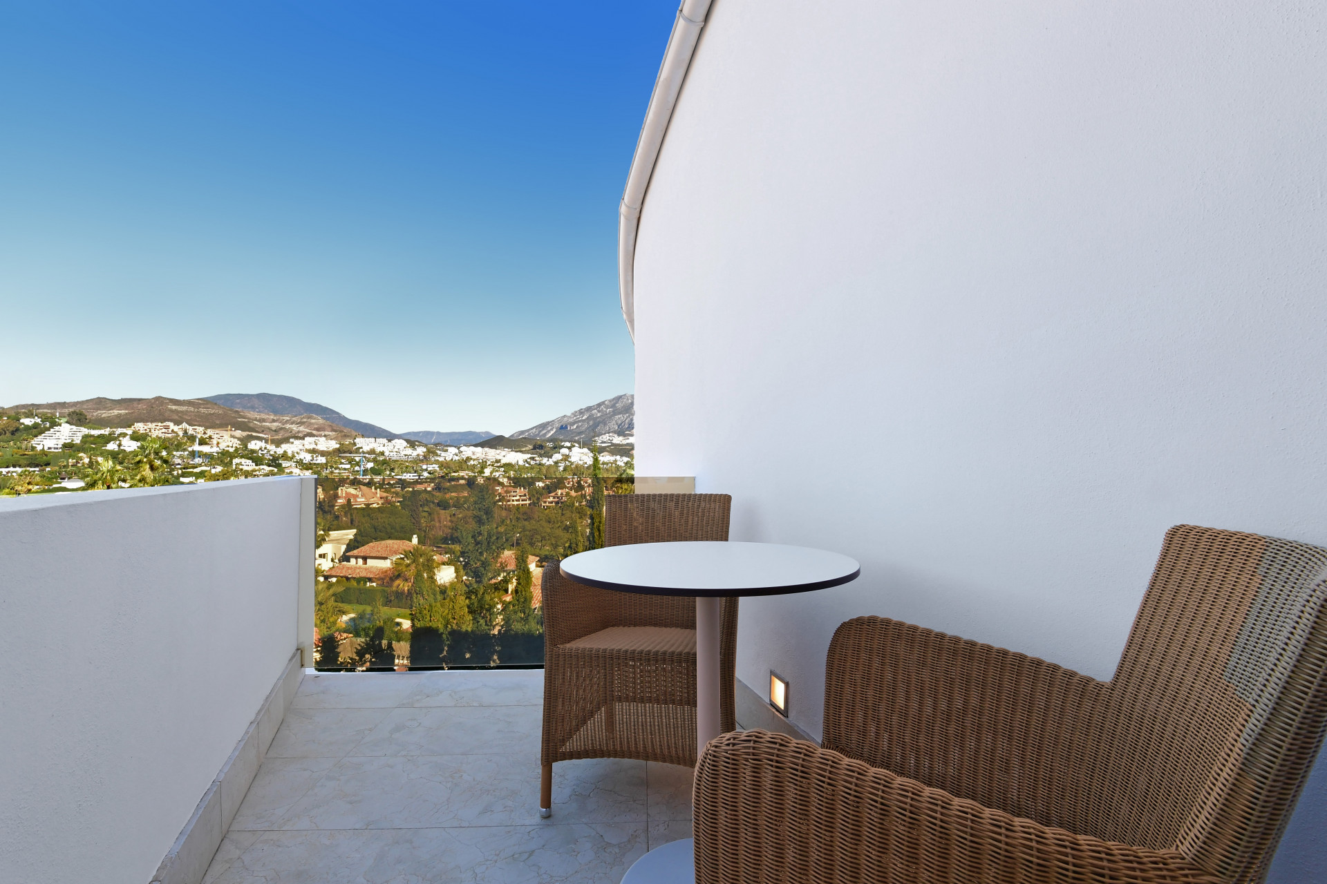Balcony with a table and chairs, offering a view of the surrounding hills and nearby houses.