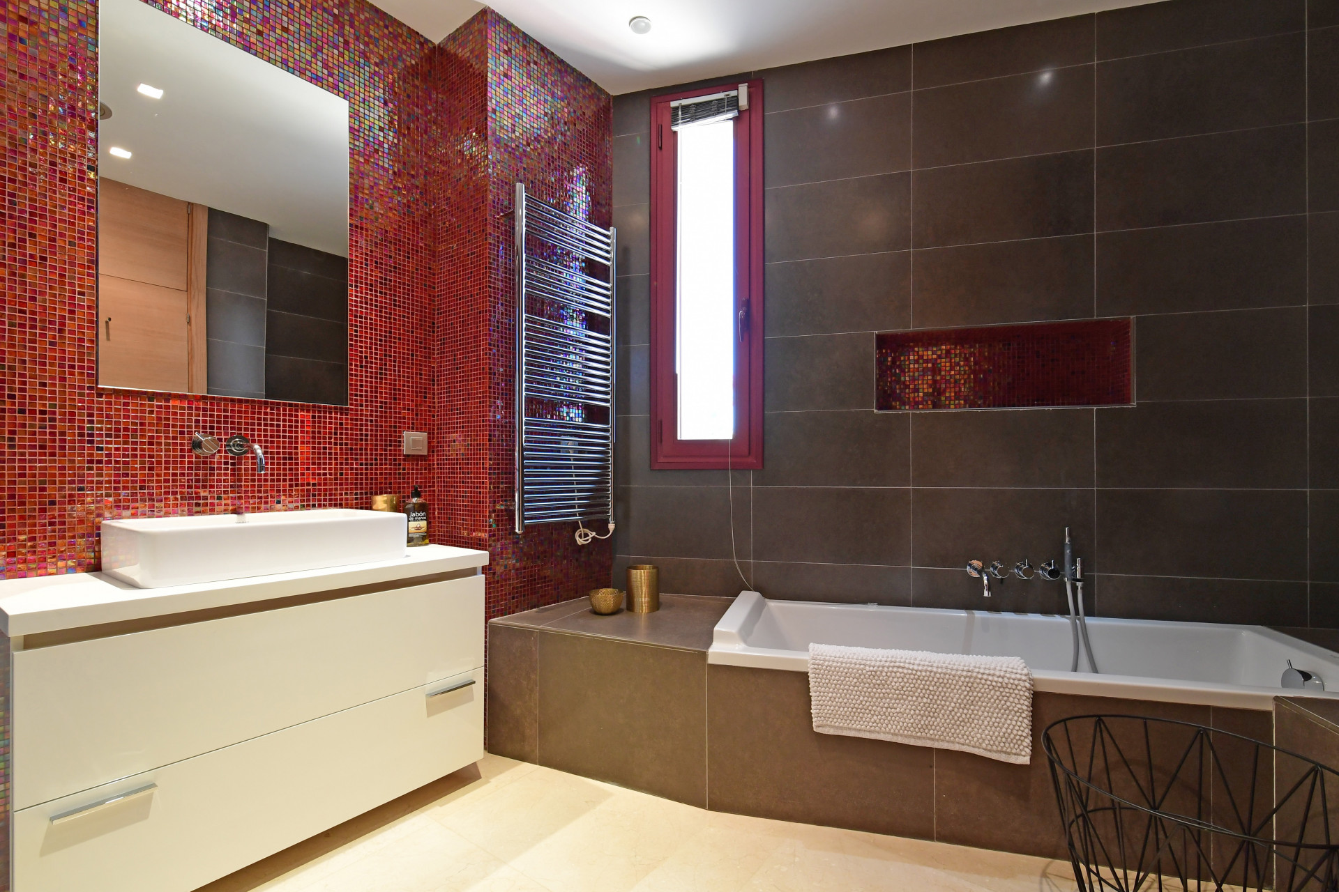 Chic bathroom with colorful mosaic tiles, modern fixtures, and a bathtub under a small window.