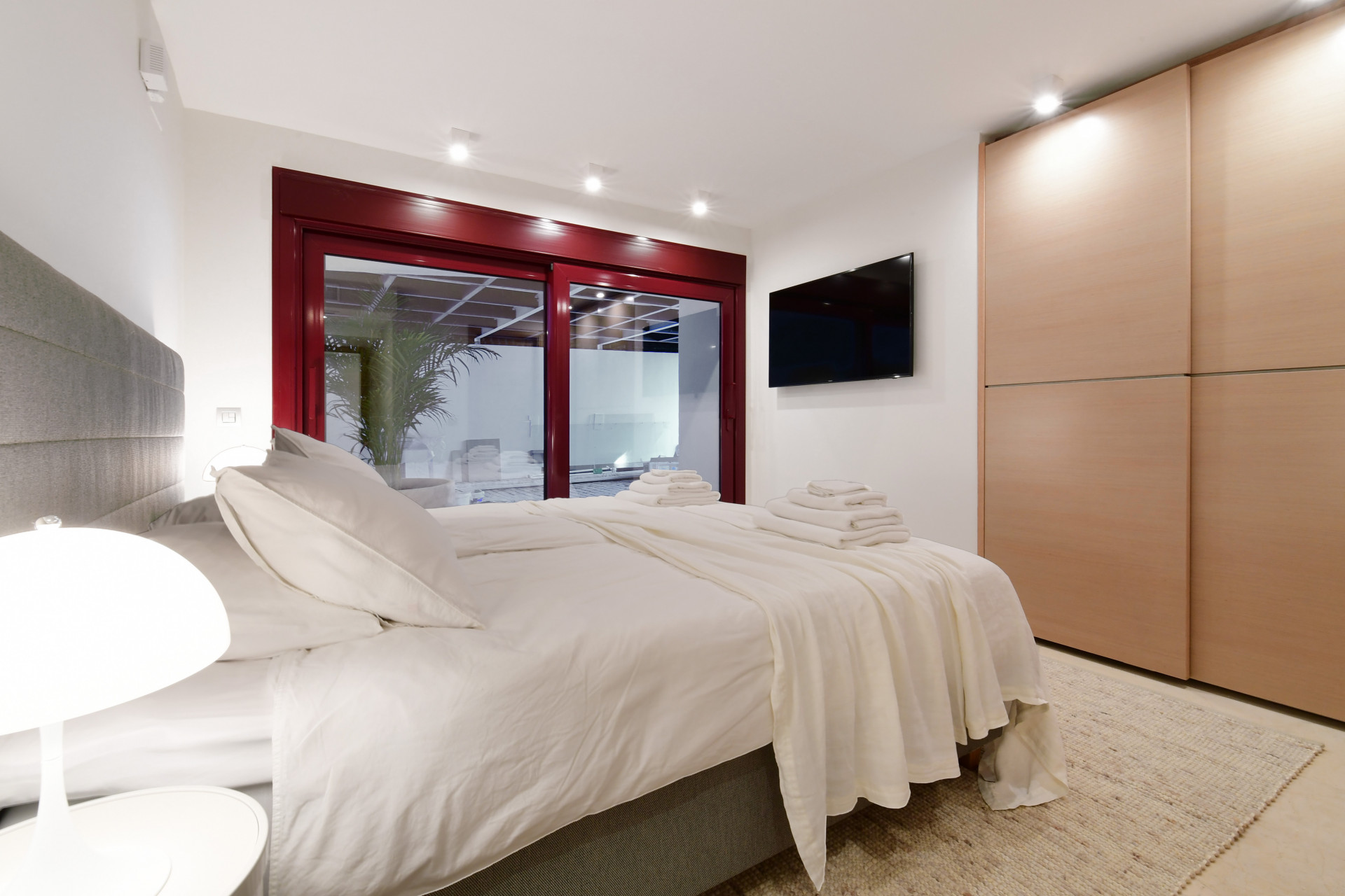 Cozy bedroom with a large bed, red window frames, and a TV mounted on the wall.
