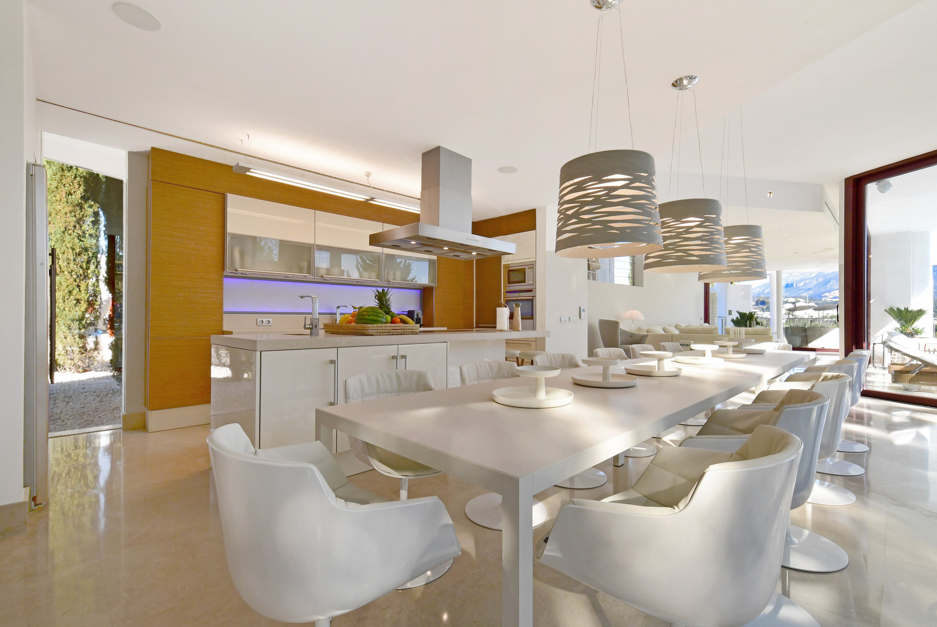 Dining space featuring a long table, pendant lights, and kitchen access.
