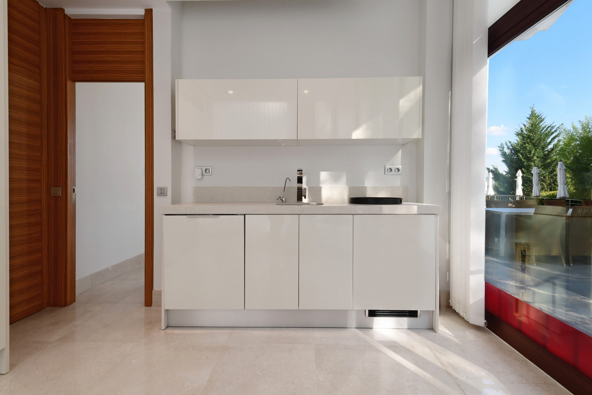 Another kitchen view showing white cabinets, a sink, and large windows overlooking the terrace.