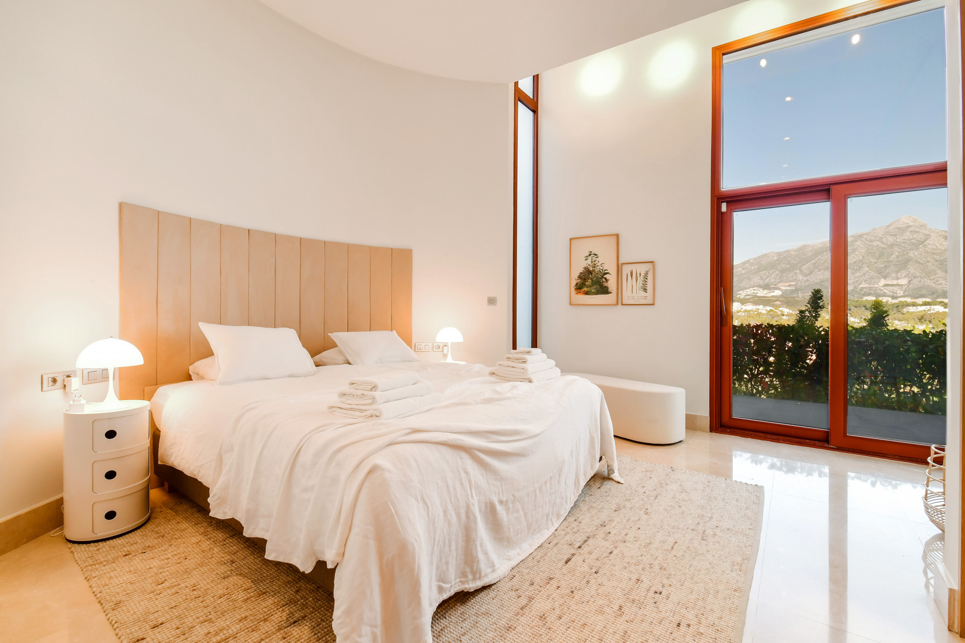 Bright bedroom featuring a large bed, soft lighting, and mountain view through the glass doors.