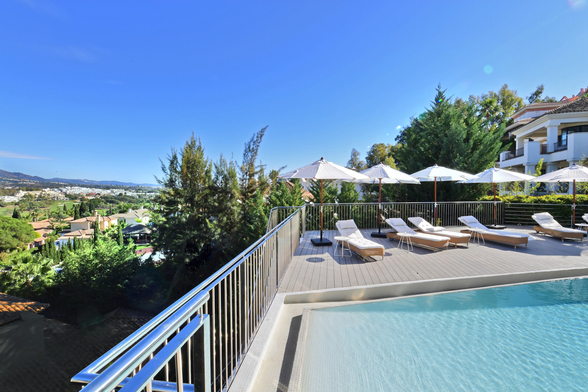 Sunlit deck area with pool loungers and views of the landscaped garden and distant mountains.