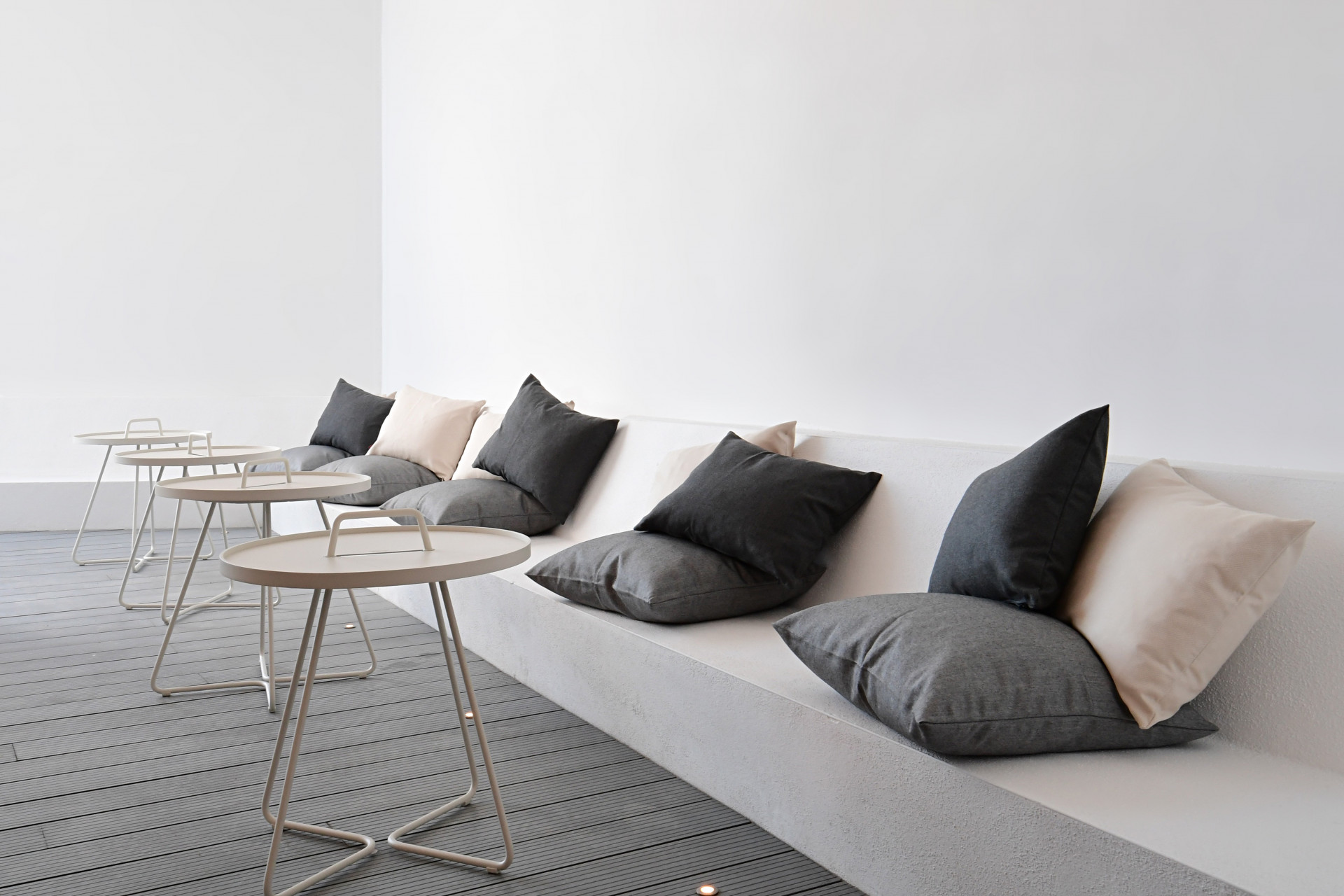 Seating area with plush cushions in varying tones, paired with light tables on a wooden decking.