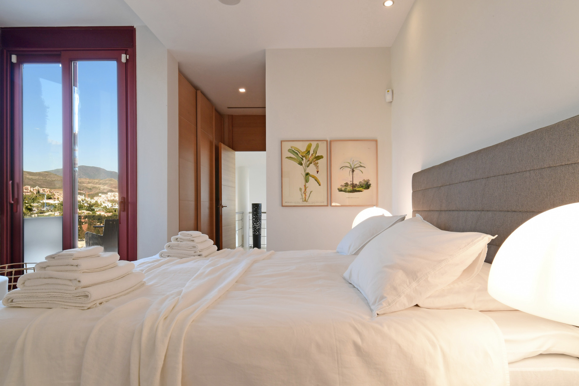 Master bedroom showcasing a grey headboard, two lamps, and wooden elements with mountain views outside.