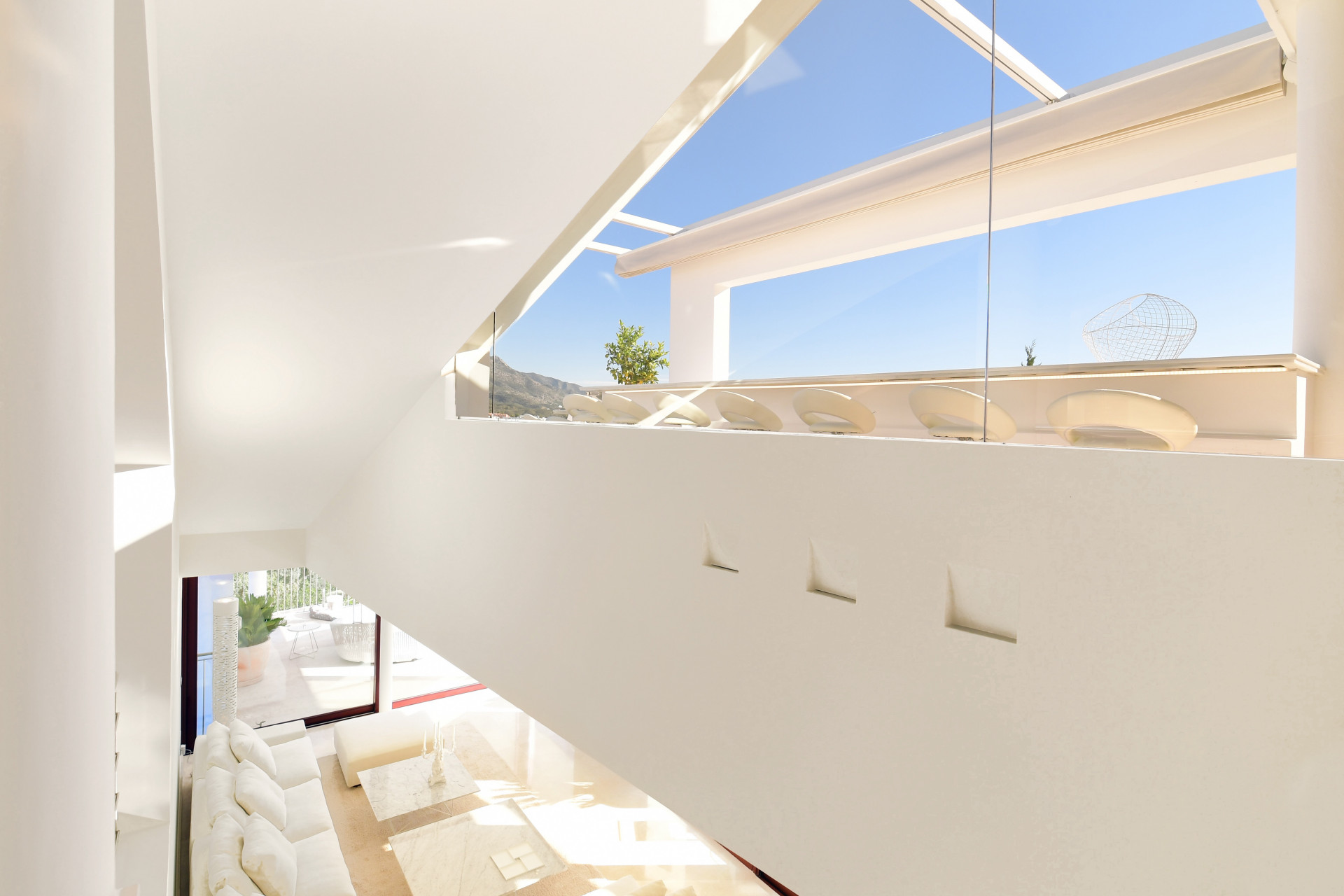 View of the spacious living area with glass railing and soft seating, showcasing high ceilings and natural light.