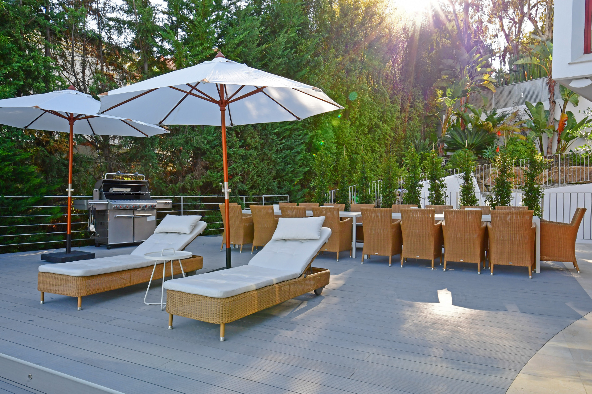 Outdoor terrace featuring lounge chairs, umbrellas, and a dining area with a grill.