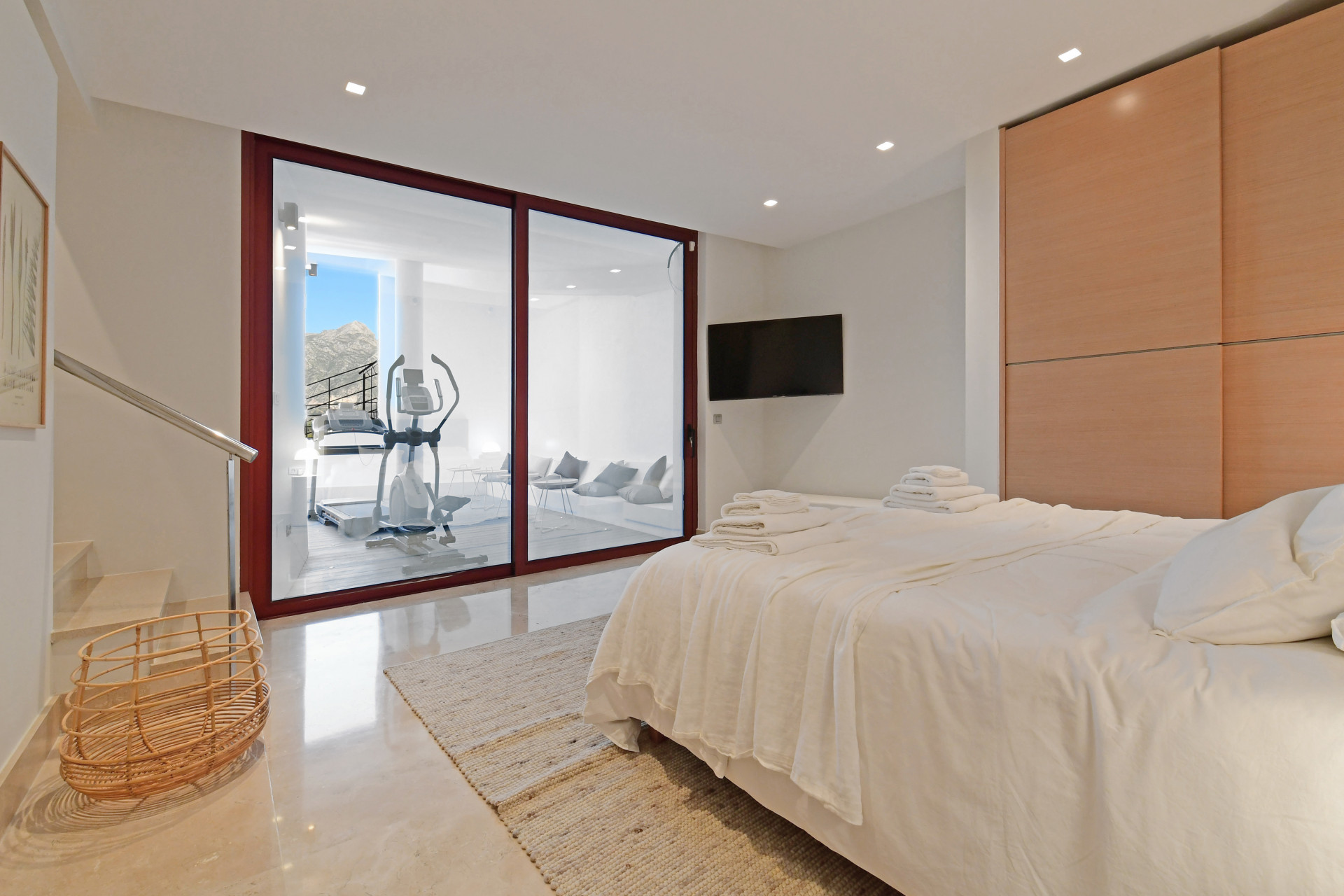 Bright bedroom with glass doors leading to a terrace, a TV on the wall, and a crisp towel arrangement.
