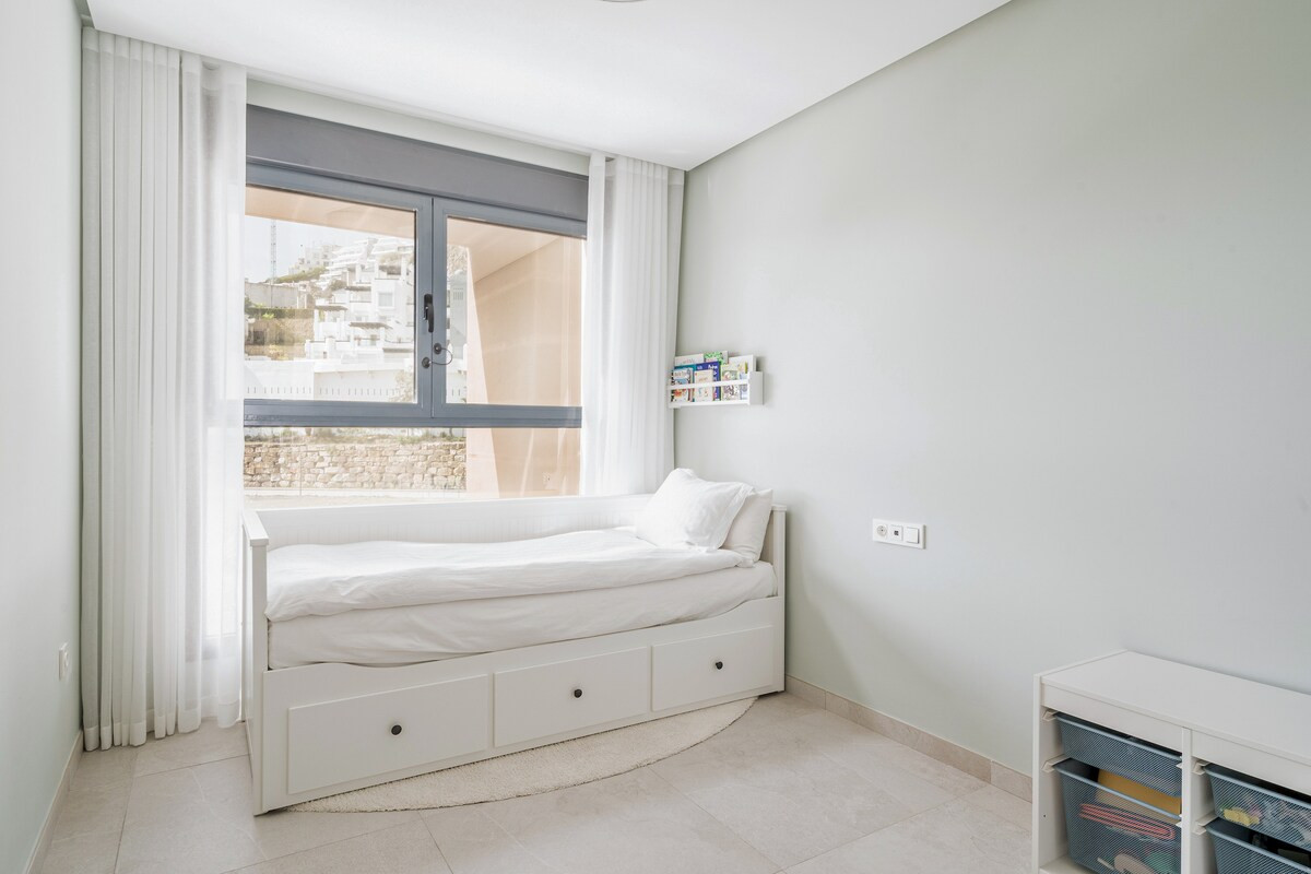 Child's bedroom with a white daybed, large window with blinds, and light green walls.