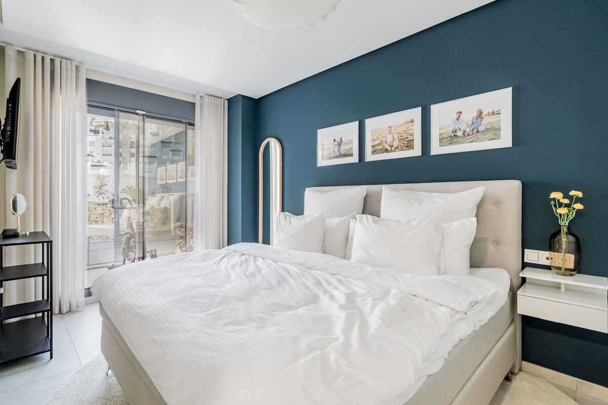 Bedroom with a large white bed, blue accent wall, and a sliding glass door to a balcony.