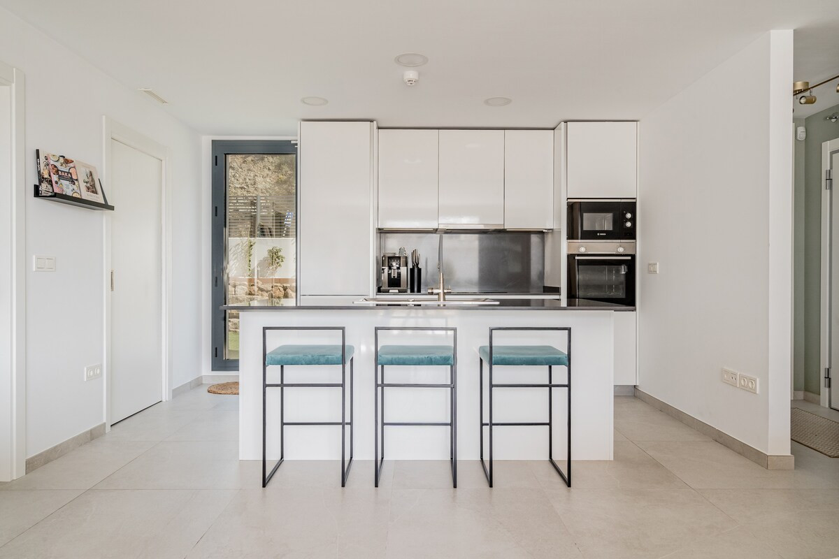 Modern kitchen with white cabinetry, stainless steel appliances, a dark counter, and three blue bar stools.