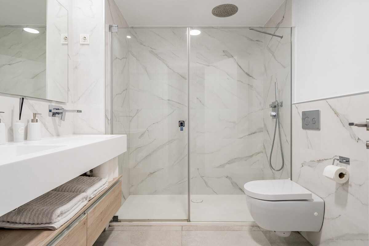 Modern bathroom with a double sink vanity, large glass shower, and wall-mounted toilet.
