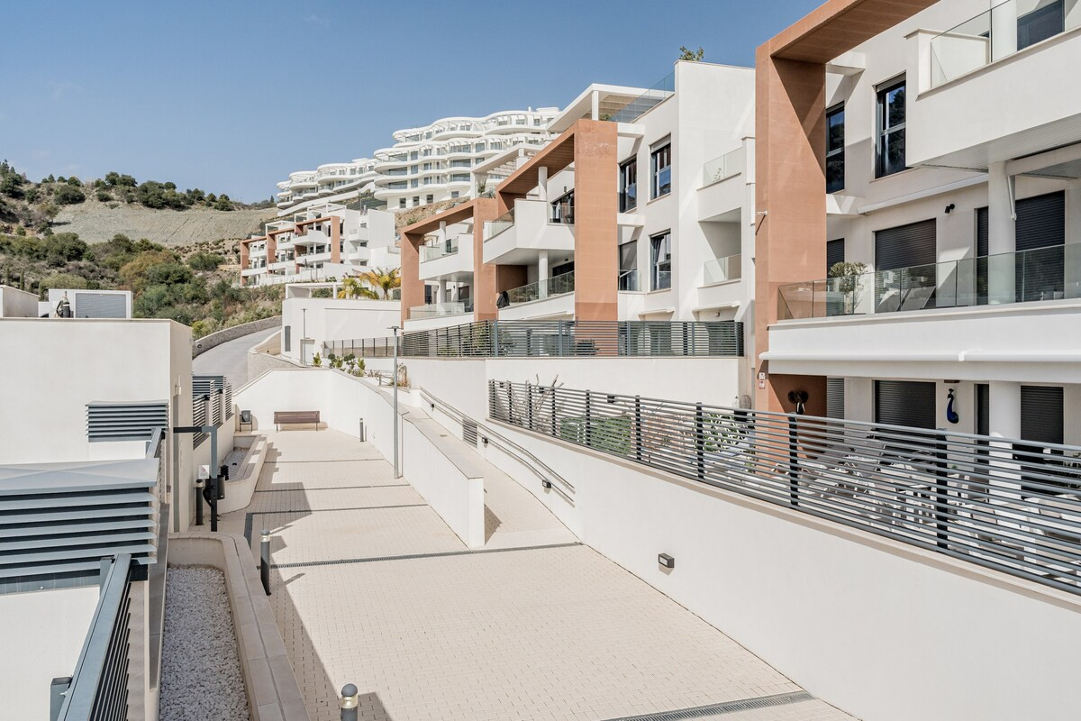 Exterior view of a modern hillside apartment complex with white facades and terracotta accents.