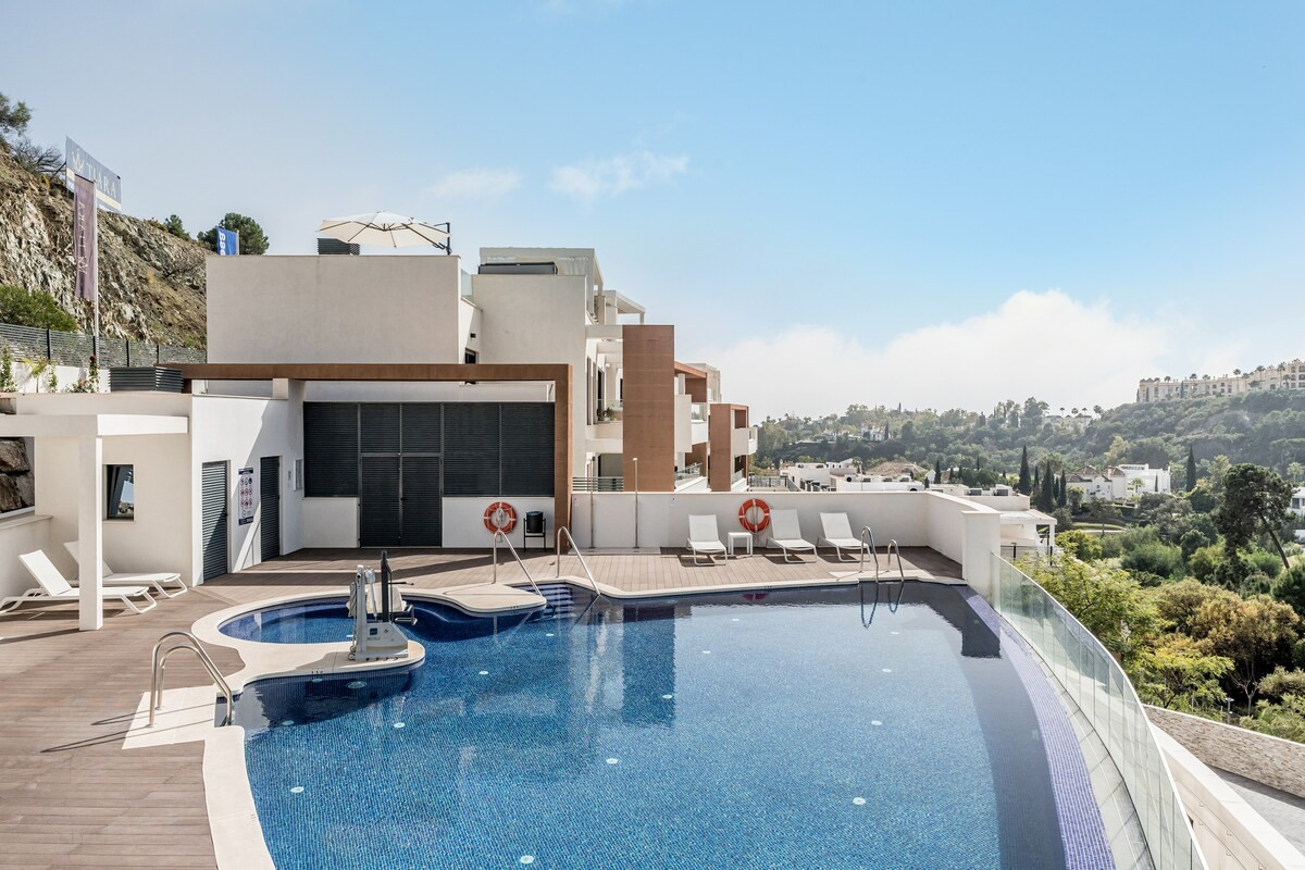 Community swimming pool with an accessible lift, surrounded by a wooden deck and modern buildings.