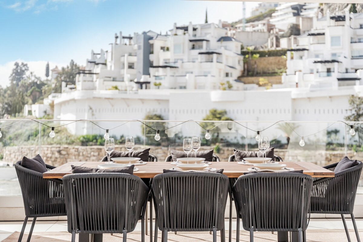 Close-up of an outdoor dining table set with plates and glasses, facing a distant hillside town.