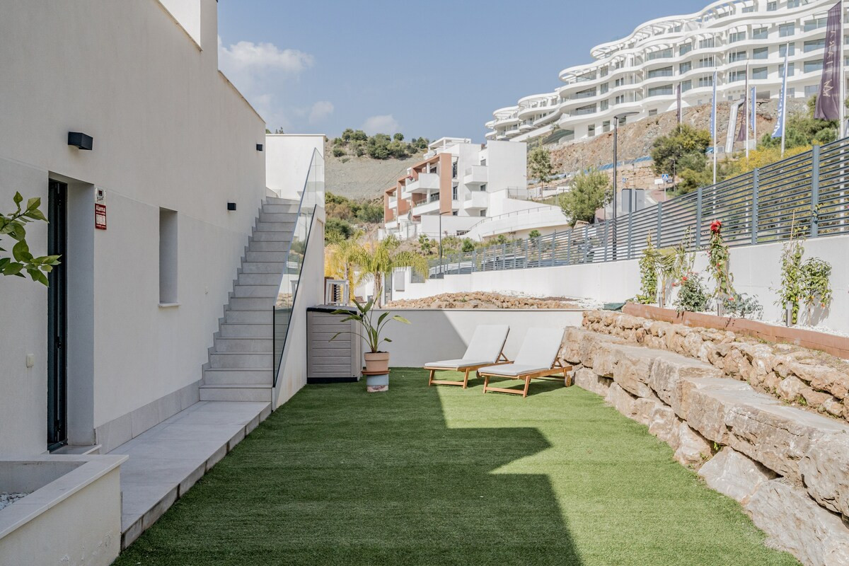 Small private garden with artificial turf, two white lounge chairs, and an outdoor staircase.