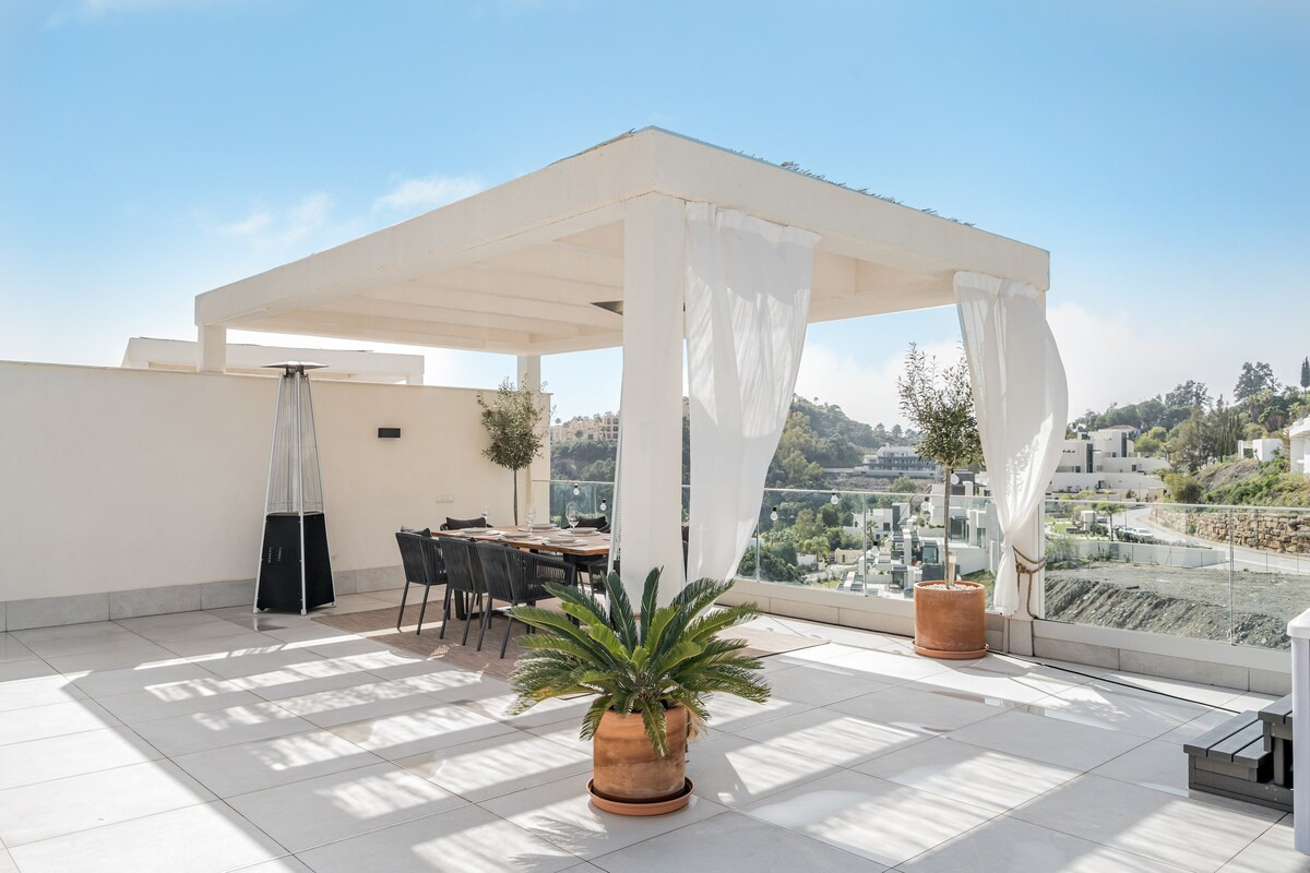 View of an outdoor covered dining area with a table set for six and two patio heaters.