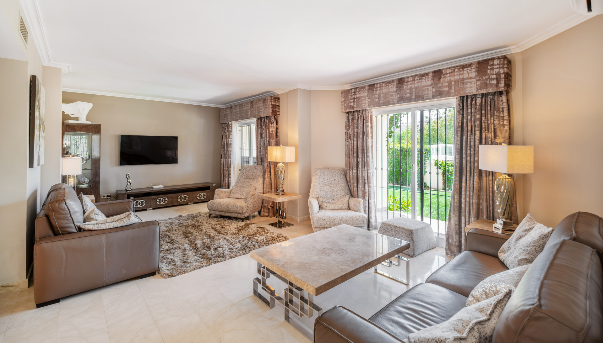 Cozy seating arrangement with a TV wall unit and large windows overlooking greenery.