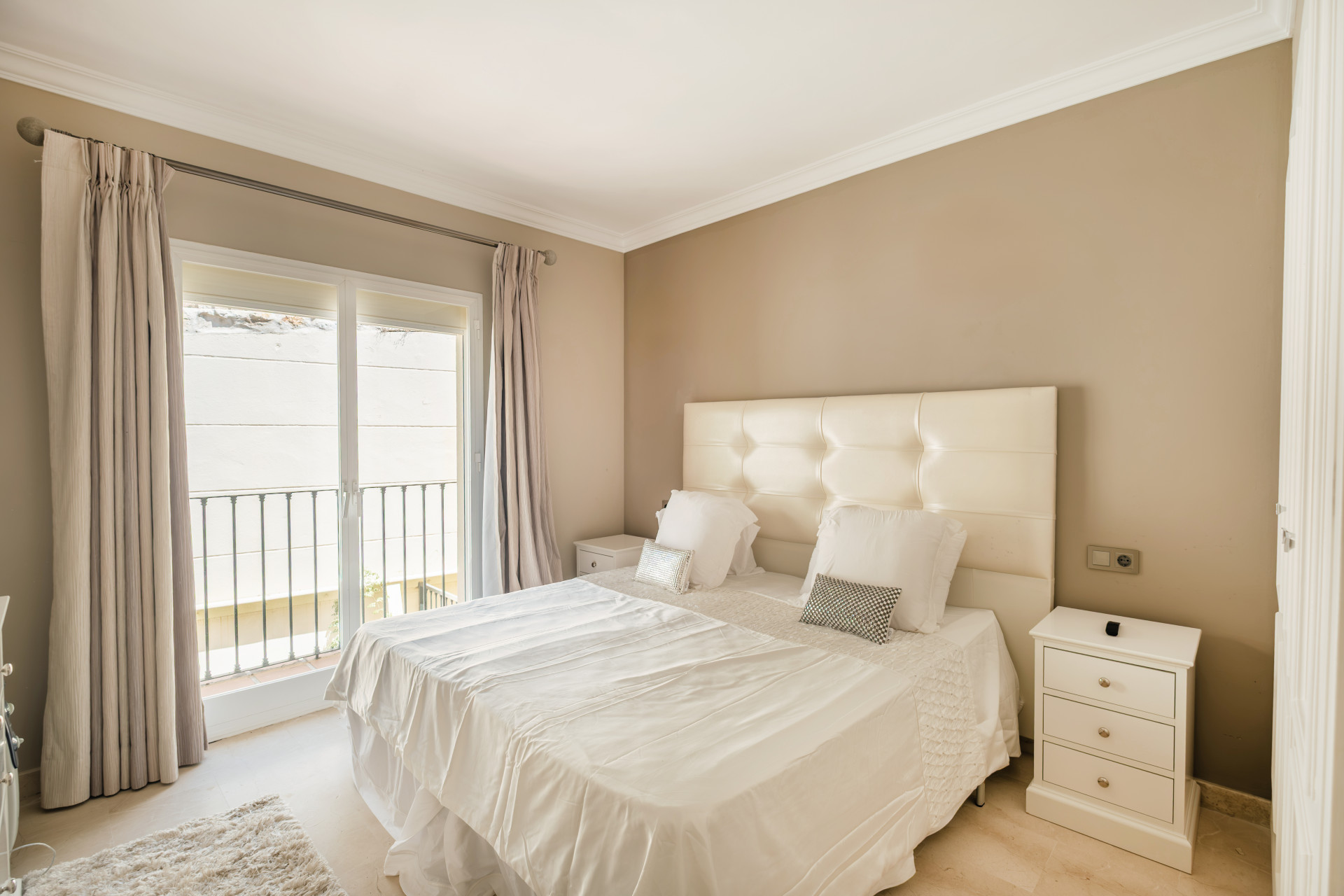 Stylish bedroom with a double bed, balcony access, and a bedside table under natural light.