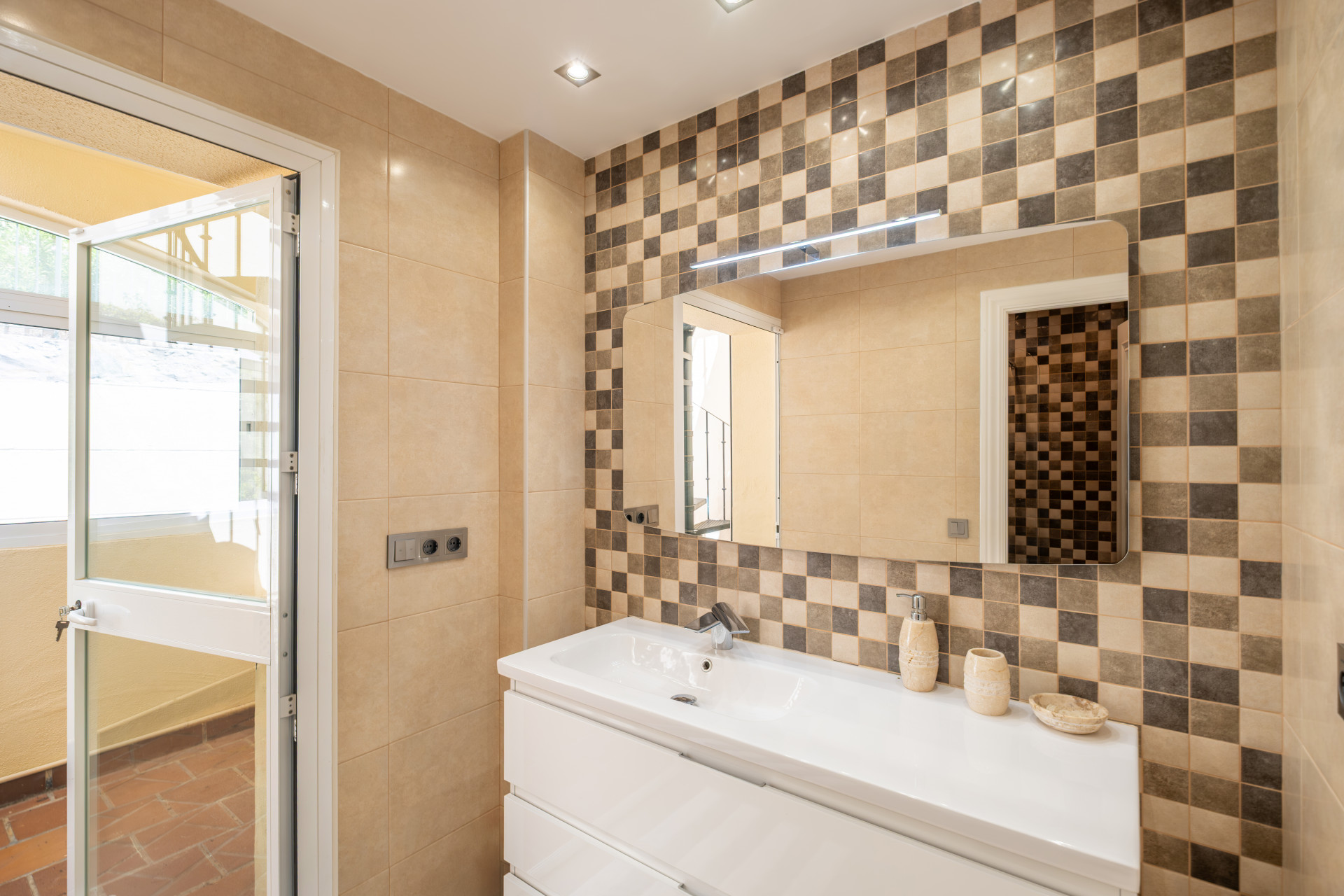 Bright bathroom with checkered tiles, a sink with storage, and a window opening to outdoors.