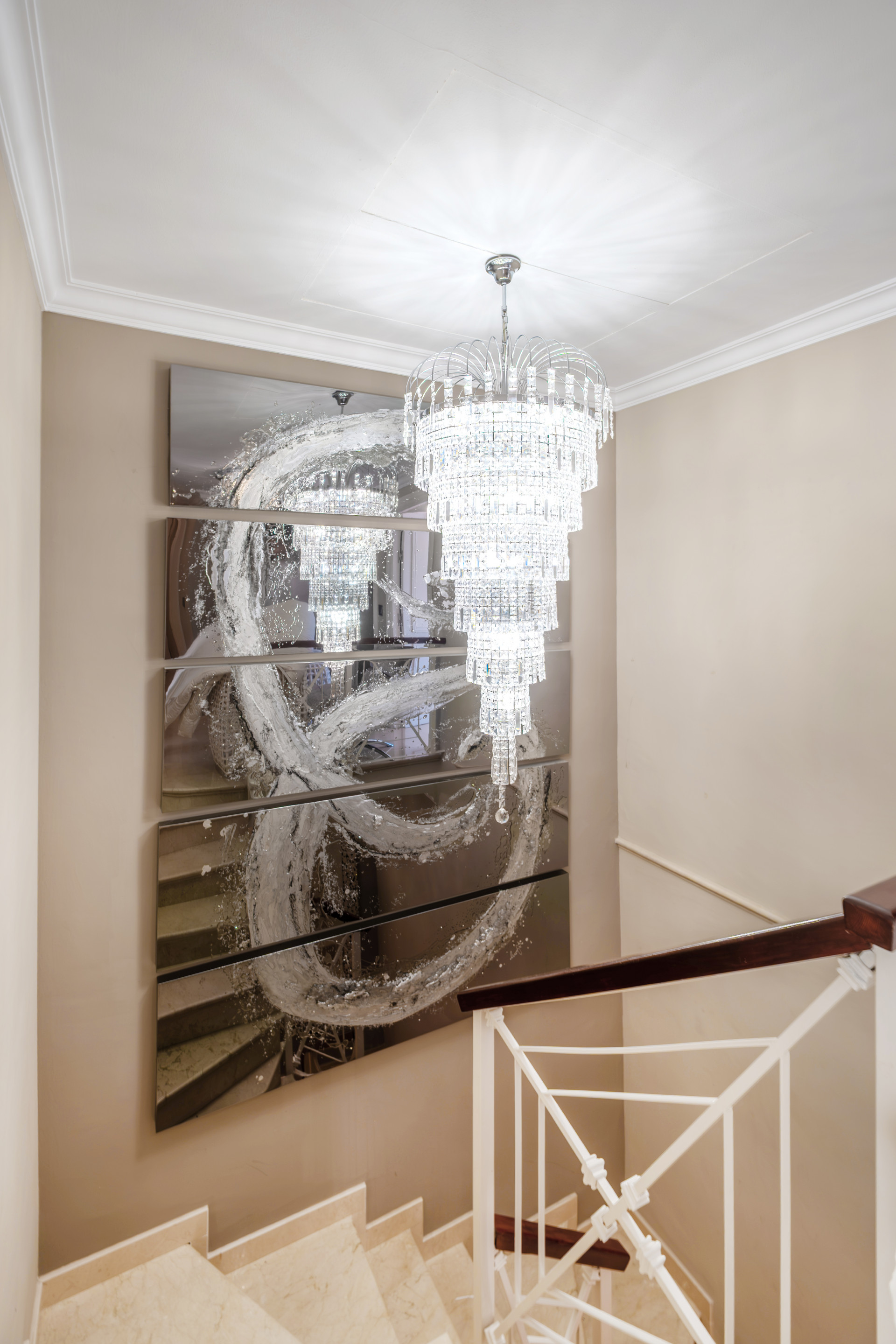 Chandelier and mirror above staircase, creating a bright focal point in the hallway.