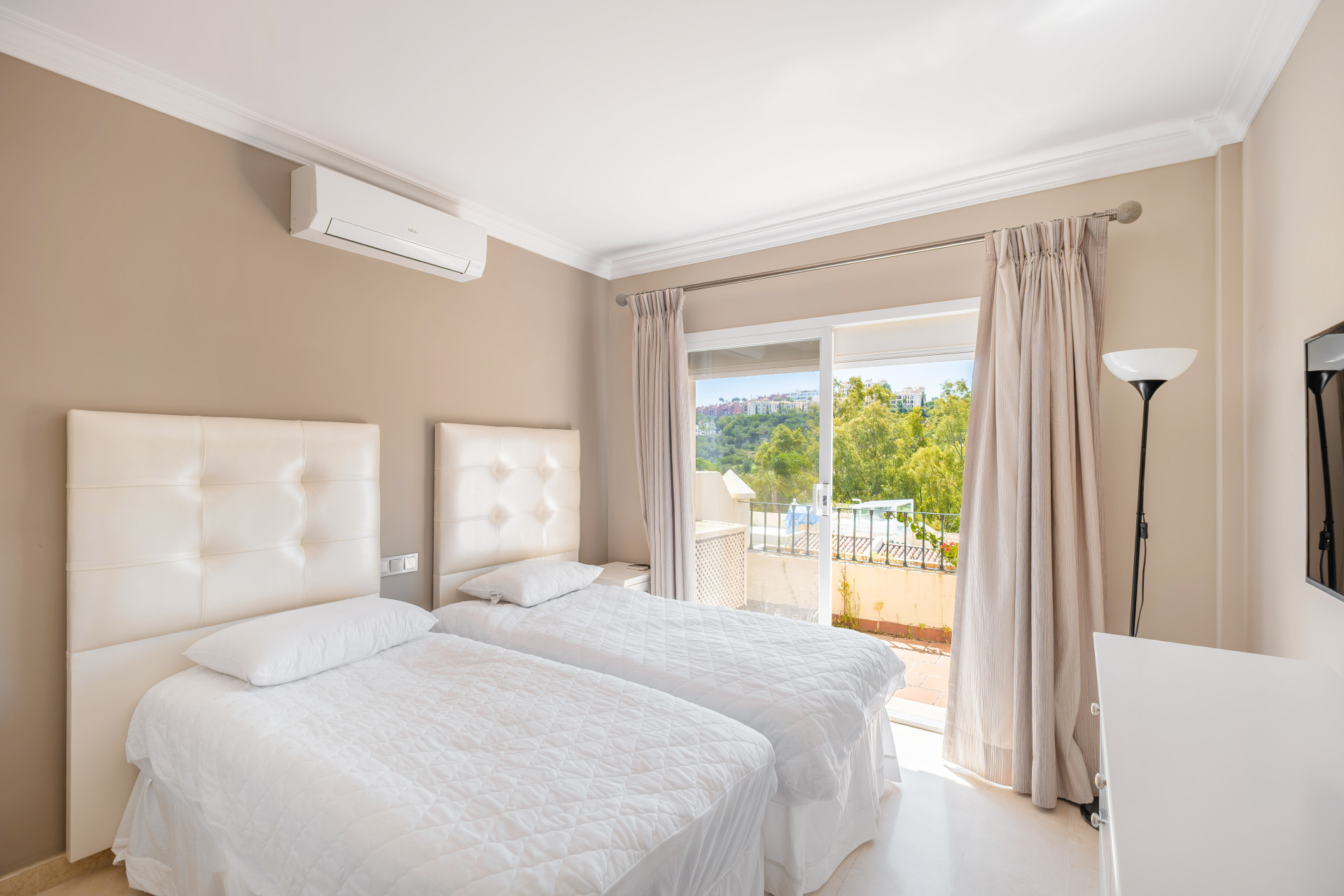 Cozy bedroom with two single beds, air conditioning unit, and a view out to a terrace through sliding doors.