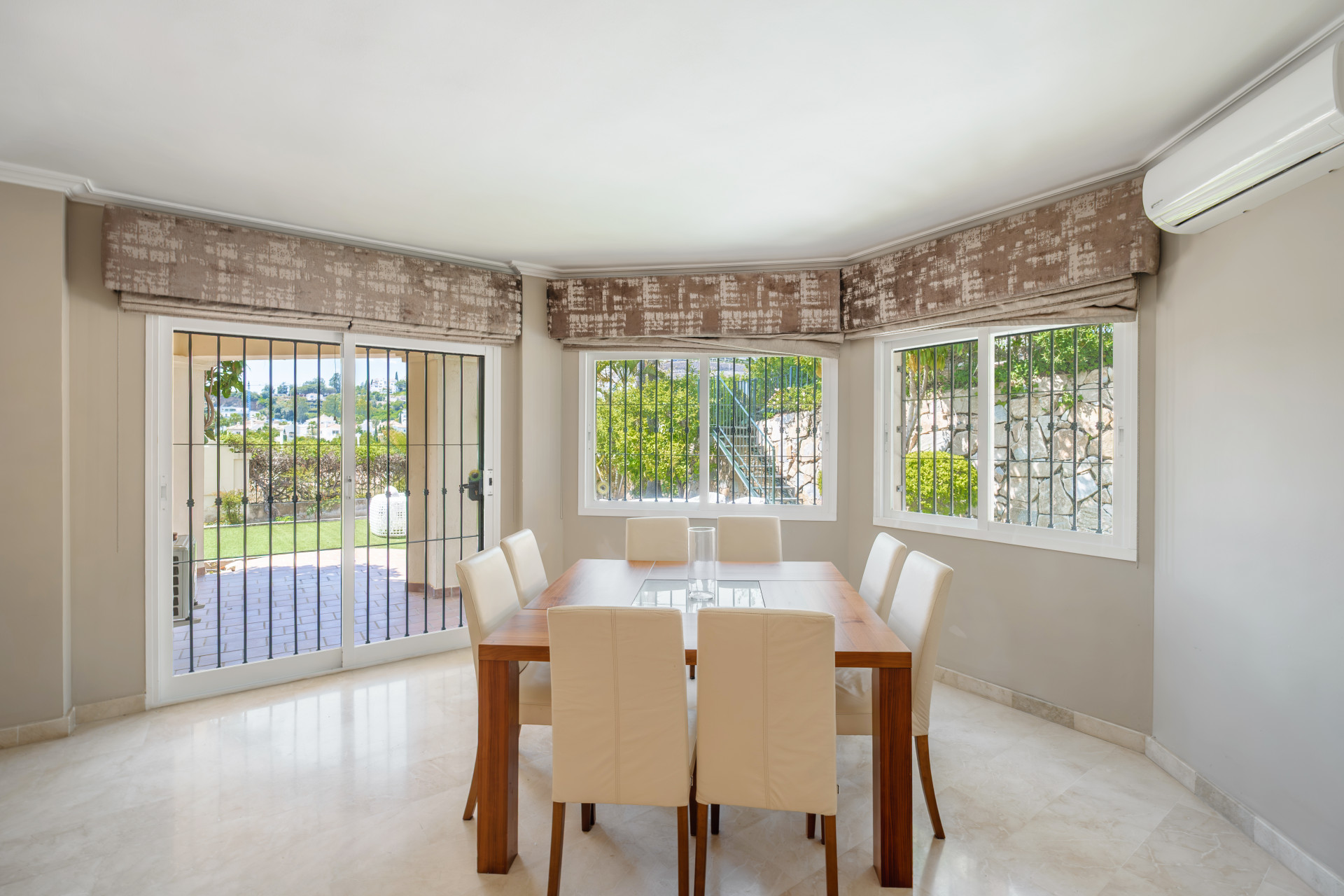 Dining area with white chairs, wooden table, and large windows providing natural light.