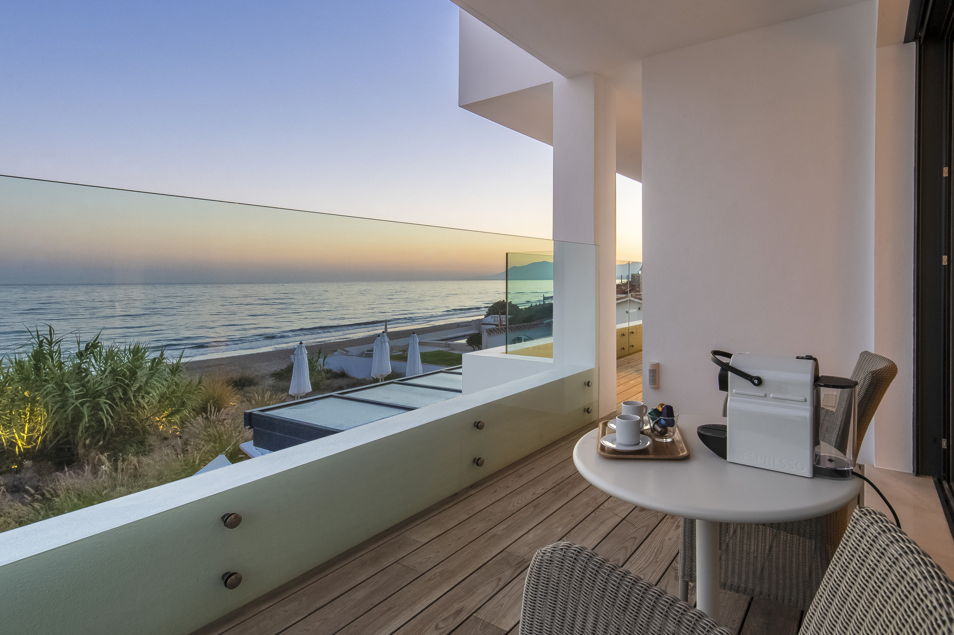 Outdoor terrace with a table, coffee setup, and ocean view at sunset.