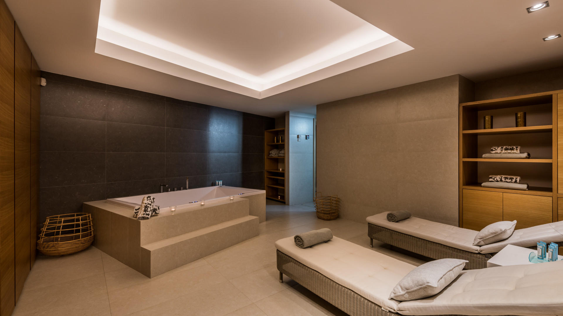 Relaxation area with a jacuzzi, loungers, wooden shelving, and subdued lighting.
