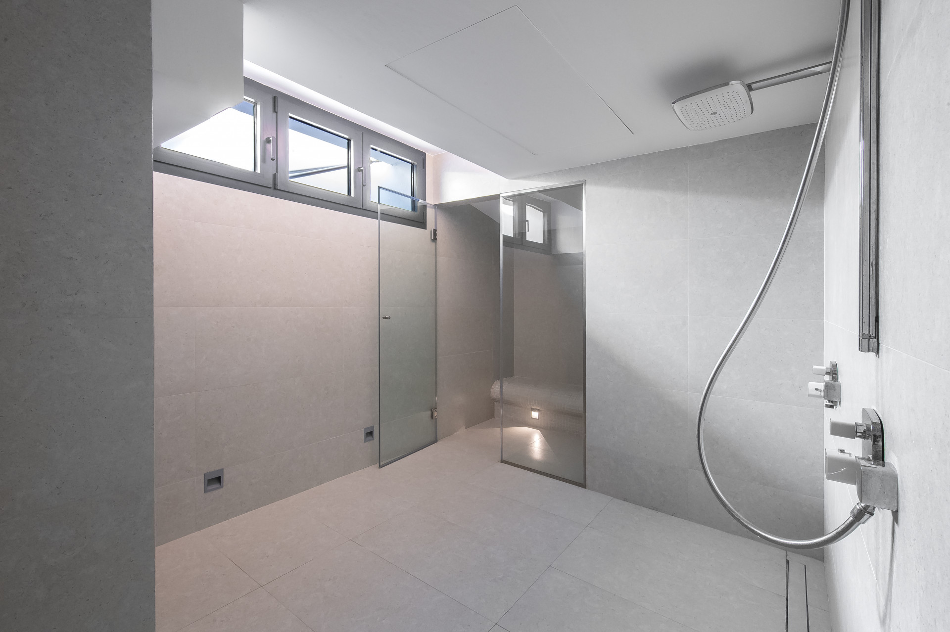 Spacious shower room with large window, neutral tiles, and glass partition.