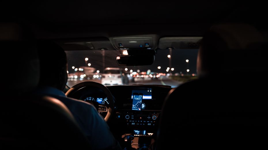 Photograph from the backseat of a taxi showing the taxi driver working at night. 