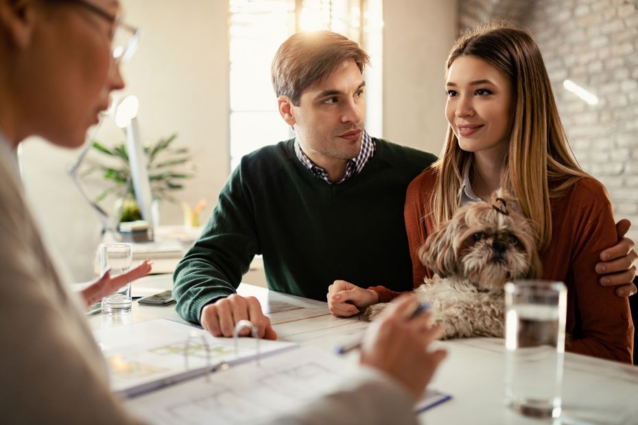 Lächelndes Ehepaar mit Hund im Gespräch mit ihrem Immobilienmakler