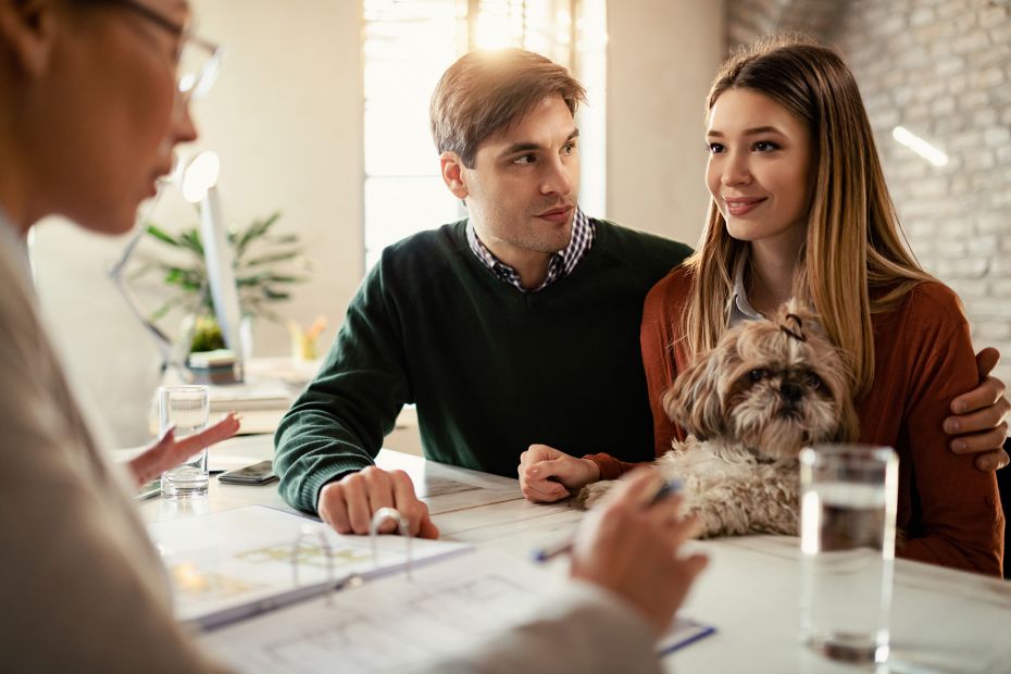 Echtpaar met een hond glimlacht terwijl ze met hun makelaar praten