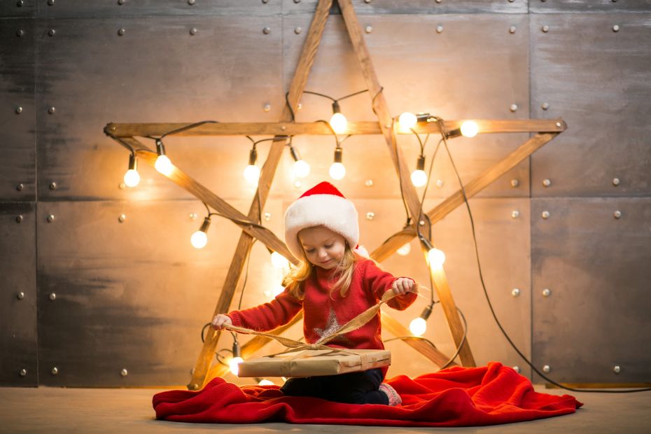 Small girl with gifts on Christmas sitting on red blanket by the star