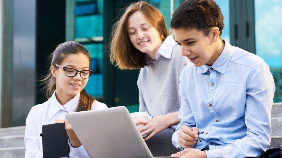 Teenage students working together with laptop at school