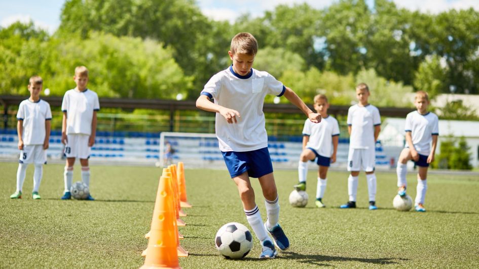 Garçons s'entraînant au football en uniforme, dans un terrain entouré d'arbres