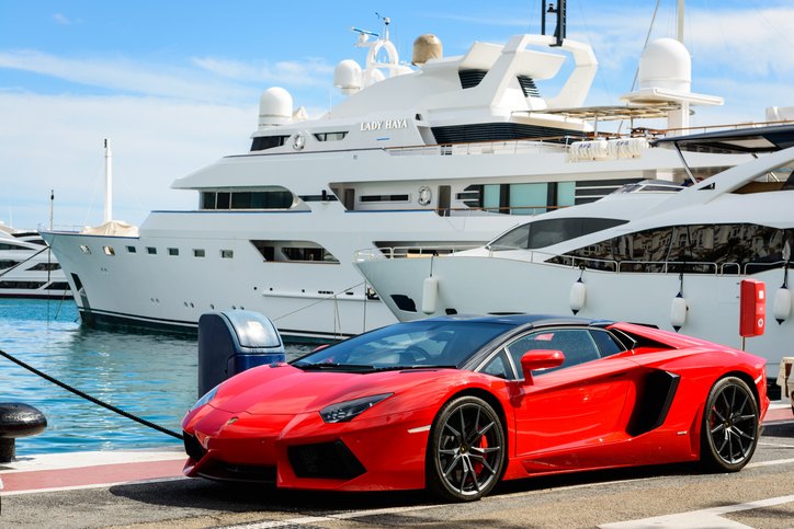 Front view of a red Lamborghini parked alongside luxury yachts in the marina of Puerto Jose Banus in Marbella, Spain.